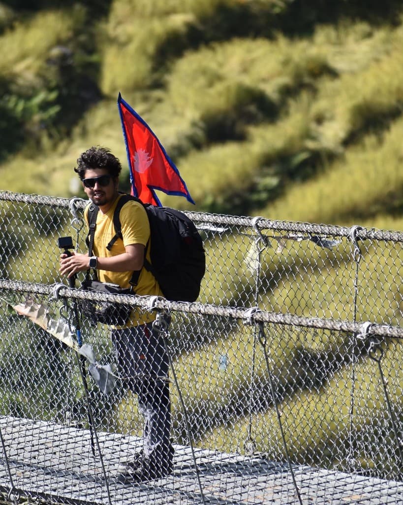 Pratap Sharma with a Nepali flag on a suspension bridge at the start of the ABC trek