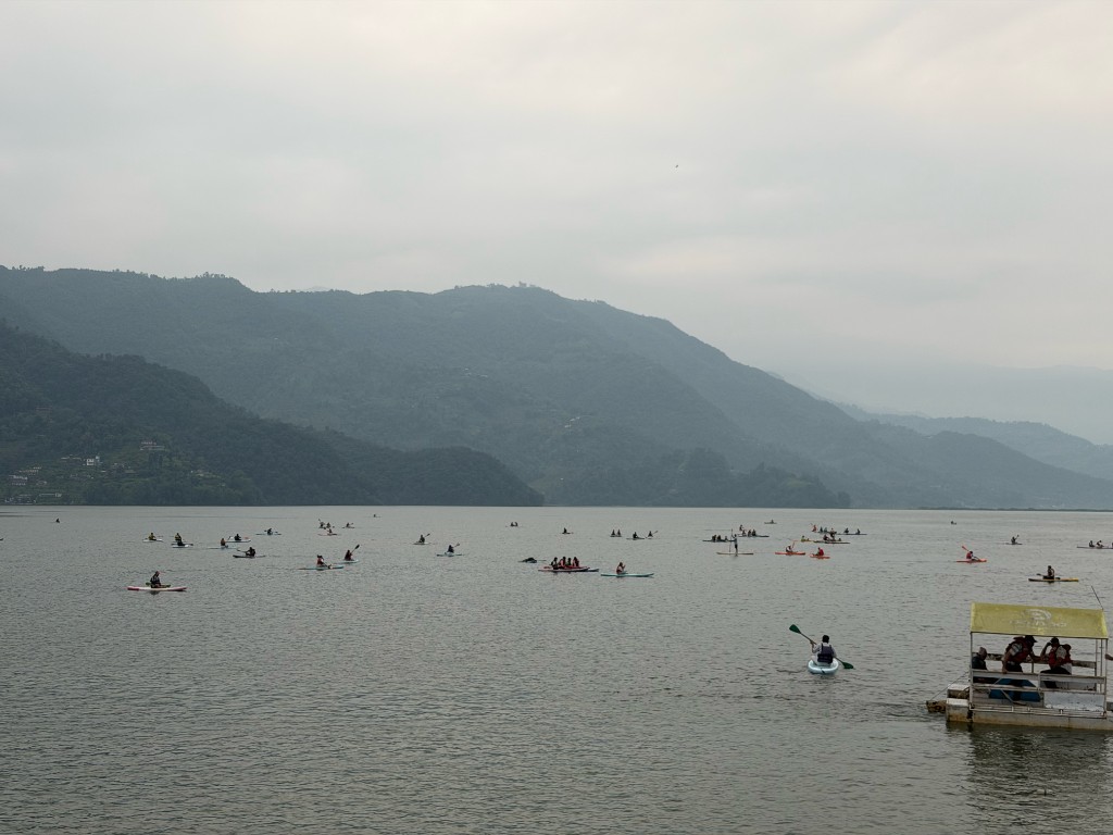 Stand-up paddleboarders on Phewa Lake with misty Himalayan hills in the background